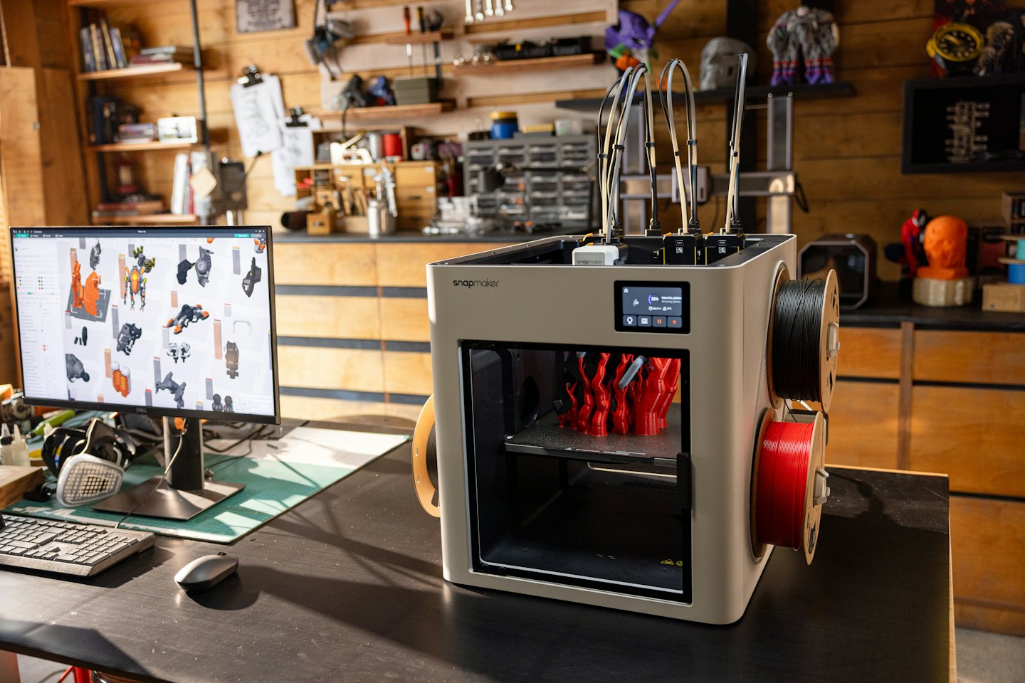 Drukarka 3D tworząca czerwony obiekt na biurku.