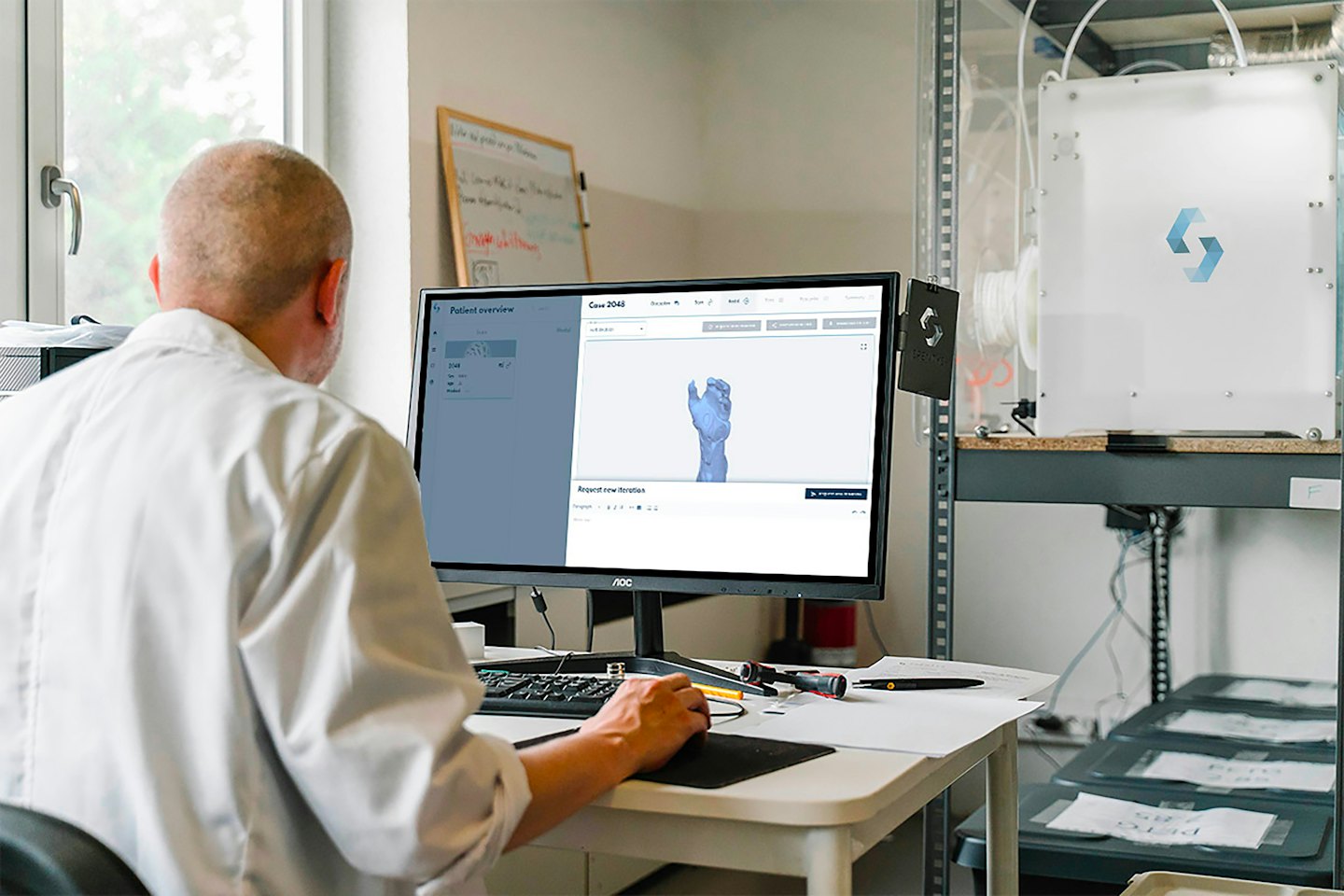 Mężczyzna w fartuchu laboratoryjnym bada trójwymiarowy model dłoni na ekranie komputera.
